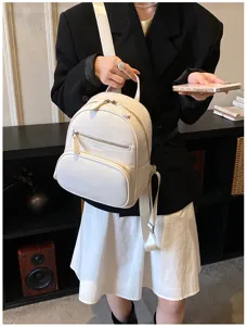 White leather mini backpack detail showing soft texture, front zipper pocket and metal hardware.
