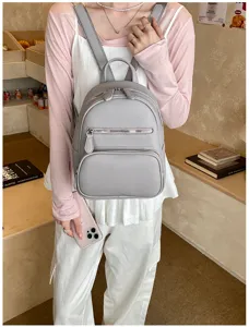 Grey leather mini backpack detail featuring front zipper pocket and fine textured material.