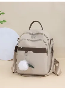 Minimalist beige backpack detail showing durable double zippers and a cute fluffy pom pom pendant.