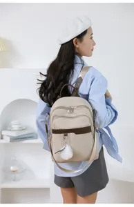 Casual minimalist beige backpack with brown trim and cute plush ball pendant for women.
