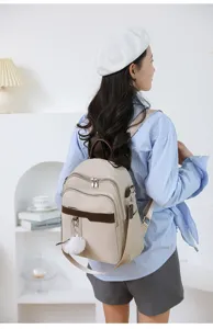 Casual beige women backpack detail view with fluffy pom-pom charm and dual zipper pockets.