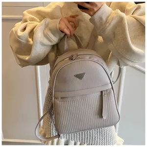 Detailed view of grey PU leather women backpack with front triangular metal badge