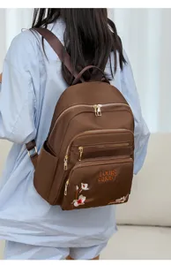 Brown nylon backpack featuring floral embroidery and gold zipper details on a model.