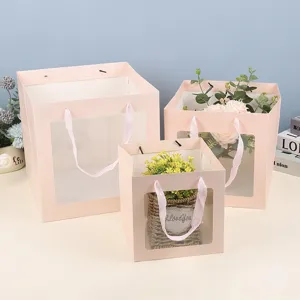 Sacs cadeaux carrés roses en papier avec fenêtres transparentes et jolis rubans élégants.
