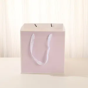 Sac cadeau en papier rose carré avec rubans blancs pour fleurs gâteaux et fêtes.