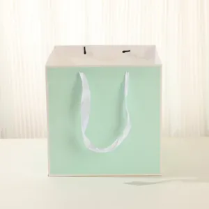 Sac cadeau vert menthe carré avec poignées en ruban blanc pour fleurs et gâteaux.
