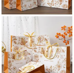 Vue détaillée de sacs cadeaux en papier à fleurs dorées avec poignées en ruban élégantes et chic.
