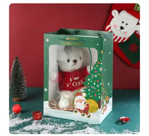 Christmas gift bag with clear window, green paper packaging with plush bear doll for holiday present.