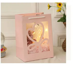 Roze papieren cadeautas met hartvenster, schattige pluche knuffel, lichtjes en opvulmateriaal.