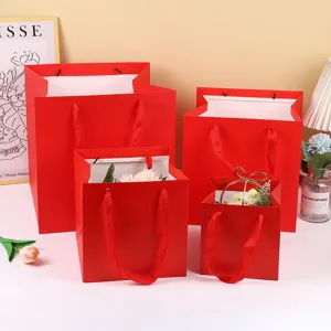 Sacs cadeaux en papier rouge carrés avec poignées en ruban pour fleurs et gâteaux.