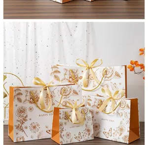 Sachets cadeaux en papier floral doré avec poignées ruban pour emballages élégants.