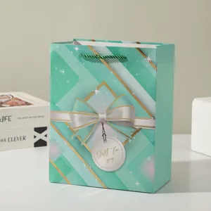 Close-up detail of mint green paper gift bag with gold geometric stripes, bow, and tag.
