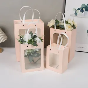 Vue détaillée de sacs cadeaux roses avec fenêtre, poignées blanches et bouquet.