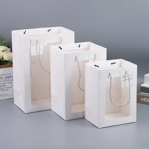 Detail view of white paper gift bags with clear window and rope handles, three sizes available.