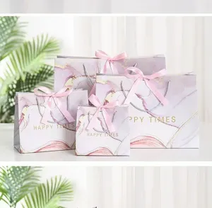 Detail view of purple marble gift bags with pink ribbon bows and gold text for party favor.