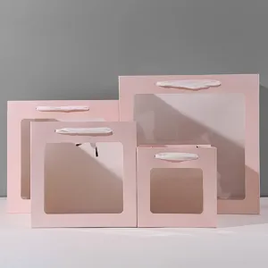 Vierkante roze papieren cadeauzakjes met doorzichtige vensters en witte lint handgrepen, voorzijde.
