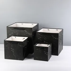 Detailed view of square marble paper gift bags with black handles and thick wide bottom.