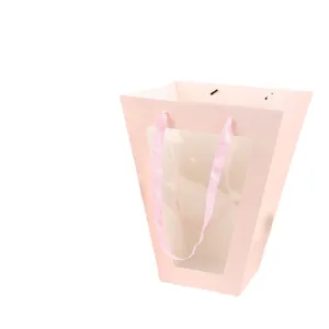 Roze trapezium vormige bloemencadeautas met doorzichtig venster en lint handgrepen.