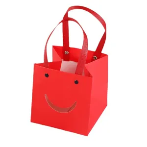 Rode papieren cadeauzak met schattig cartoon smiley gezicht en stevige lint handgrepen.