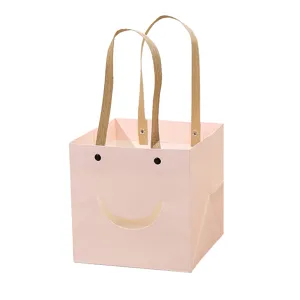 Pink square gift bag with cute smiley face cutout and sturdy handles for flower packaging.