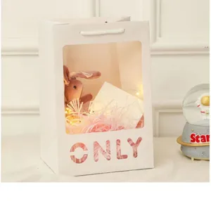 Witte papieren cadeauzak met doorzichtig venster, konijnenpop en warme lichtjes voor feest.