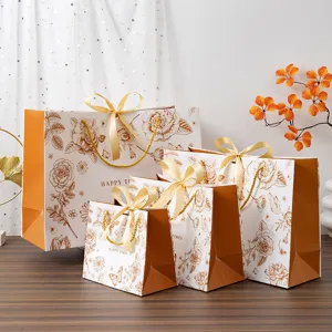 Sacs cadeaux en papier à fleurs dorées de luxe avec élégants nœuds pour emballage.