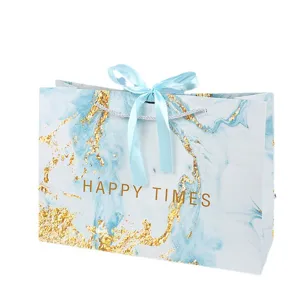 Borsa regalo di carta marmo con design dorato e nastro blu elegante per feste speciali.