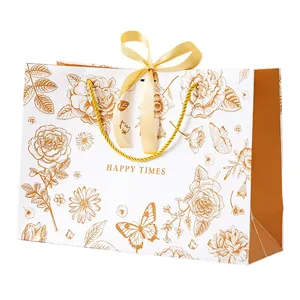 Sac cadeau floral doré avec ruban, sac en papier blanc élégant pour emballage.