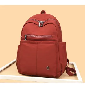 Red nylon backpack detail showcasing front zipper pocket and metal logo accent for daily use.