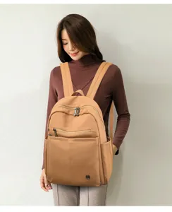 Close-up detail shot of a stylish khaki nylon backpack worn by a model, showing front pockets.