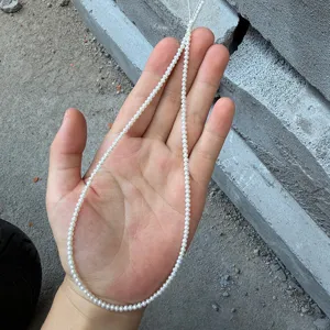 Primo piano di un mini filo di perle naturali d'acqua dolce da 2-3 mm tenuto in mano
