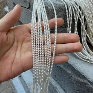 Dettaglio ravvicinato di perle naturali d'acqua dolce bianche da 2-3 mm tenute in mano