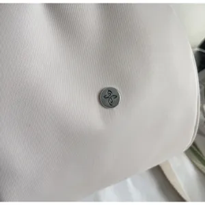 Primo piano del tessuto dello zaino e bottone metallico inciso, elegante e resistente.