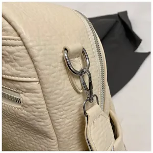 Detailed view of beige pebbled leather backpack showing silver hardware and zipper craftsmanship.
