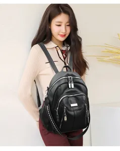 Detail view of women's black leather backpack on model, showing zipper pockets and straps.