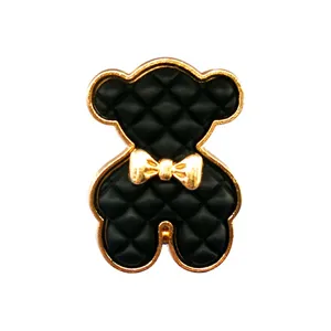 Détail de breloque chaussure ourson en métal, élégant motif matelassé noir et nœud doré.