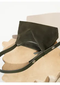 Detalle de bolso de ante verde oscuro, correa de hombro con cierre de metal elegante.