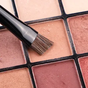 Professional makeup brush paired with multi-color eyeshadow palette for precise eye makeup application.