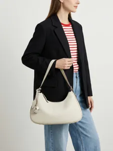 Minimalistische cremeweiße Lederhobotasche für Damen getragen von Modell im Alltag modern.