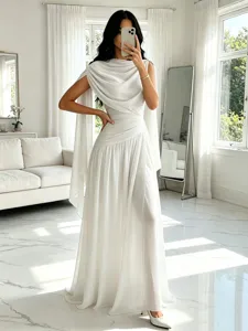 Elegante detalle de vestido largo de gasa blanca, capa drapeada en el hombro dentro de sala luminosa.