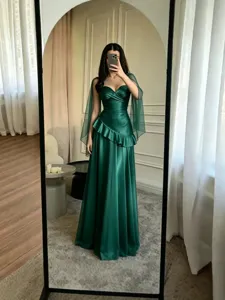 Élégante robe de soirée vert foncé sans bretelles avec volants et capes transparentes.