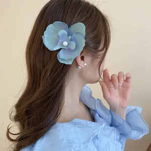 Detailed side view of a beautiful blue orchid hair clip with pearl center worn by model.