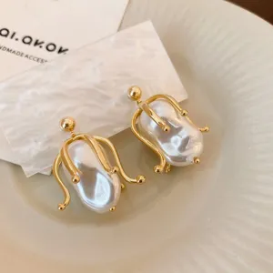 Close-up detail of baroque pearl earrings with gold-plated metal cage design, elegant aesthetic.