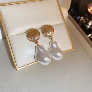 Close-up of elegant French style baroque pearl drop earrings with textured gold disk design.