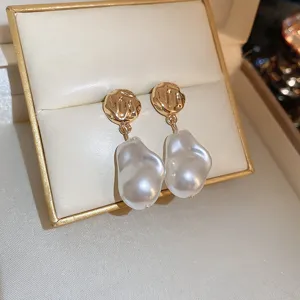 Close-up of elegant French style baroque pearl drop earrings with textured gold top detail.