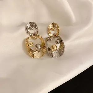 Detailed close-up shot of asymmetric metallic drop earrings with double circles and shiny spheres.