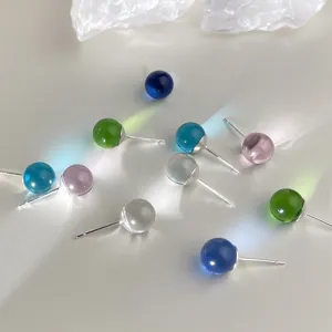 Close-up detail of colorful translucent glass ball stud earrings with shining light reflection.