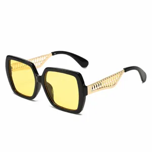 Occhiali da sole quadrati alla moda con montatura nera lenti gialle e aste dorate traforate.