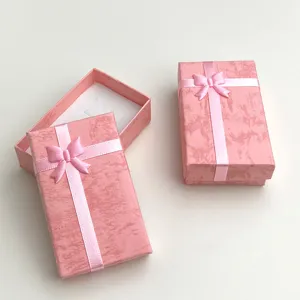 Dettaglio scatola regalo per gioielli rosa con superficie in carta testurizzata e fiocco.