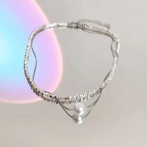 Close-up detail of silver faceted beaded layered necklace with a pearl pendant on mirror.